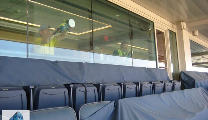 Richard Evans and union helper resurfacing tempered glass panels inside Notre Dame Stadium, viewed from exterior looking through glass