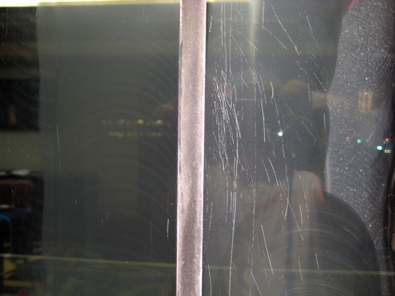 Close up showing severity of scratches on commercial glass restoration project at Notre Dame